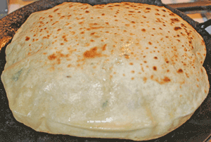 Roti flipped to cook other side, continuing to rise on tava/pan.Rotis gently pressed with a spatula to increase rising of roti