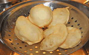 Fried Puris being scooped from oil in large ladle with holes