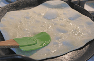 Rotis cooking being pressed with a spatula to increase rising of roti